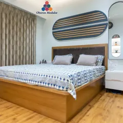 This modular bed, finished in a warm veneer with a comfortable upholstered headboard, is the centerpiece of this bedroom. The design is complemented by a custom wall art piece and a sleek white PU finish bedside unit.