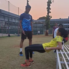 A coach supervises an athlete performing a hip thrust on a bench. This exercise is one of the best for strengthening the glutes, which are crucial for power in running, jumping, and changing direction.
