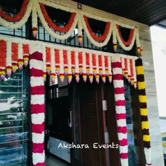 A vibrant floral decoration for a housewarming ceremony main entrance. This design uses thick garlands of white, red, and orange flowers with lotus bud details to create a warm and welcoming entryway.