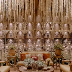 A grand seating area set against a backdrop of tiered, candle-lit alcoves. The ceiling is adorned with a cascade of white floral strings, creating a breathtaking effect of falling snow or stars.