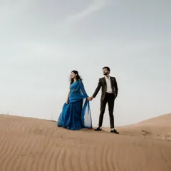 The sweeping dunes of the desert create a dramatic and romantic setting. The bride's flowing blue saree provides a stunning contrast against the sand.