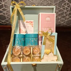 A closer look inside the elegant Diwali trunk hamper. It includes two decorative tins, a handmade tea cake, and a box of beautiful diyas, all tied with a golden ribbon.
