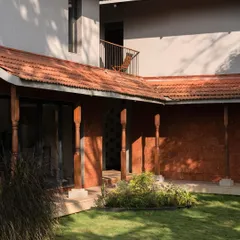 The courtyard of Maison Rouge, featuring reclaimed timber columns and a laterite stone wall. This space is the heart of the home, connecting the different living areas.