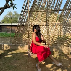 A candid moment on a swing, showing off the vibrant color of this red spaghetti-strap dress. This is a versatile piece that can be dressed up or down for any fun occasion.