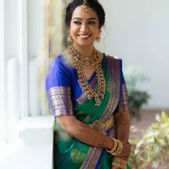 A candid moment of joy. This bride's radiant smile is enhanced by a soft glam makeup look, featuring defined eyes and a natural lip tone that harmonizes with her beautiful green and blue silk saree and antique-finish jewellery.