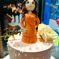 The custom figurine placed on top of an elegant pink cake, decorated with pearls and fresh white roses. The topper becomes a cherished keepsake from the celebration.