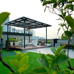 A view through the greenery of a simple yet elegant black metal pergola. It creates a defined, raised seating deck on the terrace, separating the lounge from the lawn area.