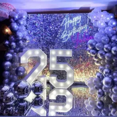 A glamorous 25th birthday backdrop featuring a silver sequin wall that sparkles and shines. The setup is completed with a custom neon sign, marquee numbers, and a silver balloon garland.