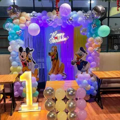 A classic Mickey Mouse and friends theme for a first birthday. This setup includes character cutouts of Mickey, Pluto, and Donald Duck, a colorful balloon arch, and a light-up number '1'.