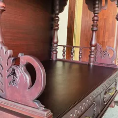 A close-up of the side of a custom mandir, highlighting the hand-carved peacock motif and the detailed railing. The rich mahogany finish adds to its traditional and elegant feel.