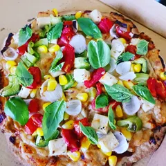 A vibrant millet base pizza topped with fresh basil, corn, bell peppers, and cubes of millet cheese. A true celebration of the year of the millet.