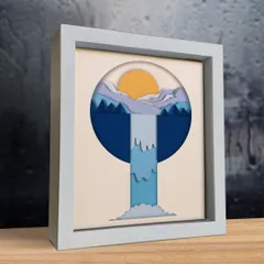 The waterfall shadow box is shown here in a white frame, placed on a wooden shelf. Its compact size makes it perfect for adding a touch of nature to any small space.