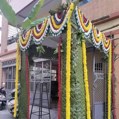 A simple and elegant 'chapra' for a home entrance, made from woven coconut leaves and decorated with colorful flower garlands and banana leaf stalks.