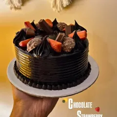 A decadent Chocolate Strawberry cake, perfect for the ultimate chocolate lover. It's adorned with chocolate swirls, Ferrero Rocher, and fresh strawberries.
