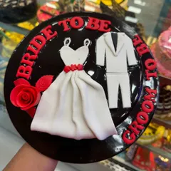 A classic 'Bride to Be' and 'Groom to Be' cake. This chocolate cake is decorated with a fondant wedding dress and suit, making it a perfect centerpiece for a pre-wedding celebration.