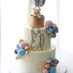There's nothing sweeter than celebrating a new beginning. This two-tiered baby shower cake features a dreamy hot air balloon with a tiny teddy bear, all handcrafted from fondant, surrounded by a cascade of pastel chocolate spheres. It’s a gentle and elegant way to welcome a little one.