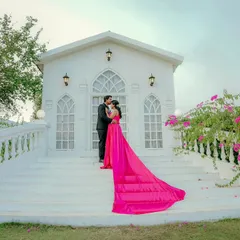 A dramatic and breathtaking shot. The bride-to-be's vibrant pink gown flows down the steps of a beautiful white chapel, creating a truly cinematic pre-wedding moment.