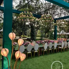 An outdoor setting offers a beautiful canvas. For this lakeside reception, we designed a long, mirrored dining table adorned with lush floral runners and surrounded by elegant seating, creating a serene and magical dining experience under twinkling lights.