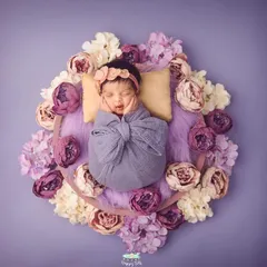 Capturing a tiny, sleepy smile is the best reward. This newborn is beautifully swaddled and surrounded by a wreath of purple flowers, showing our attention to color and detail.