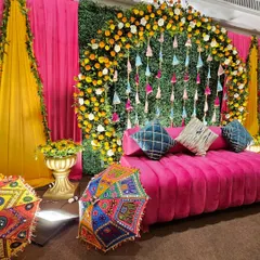 This vibrant Mehendi setup captures the joyful spirit of pre-wedding celebrations. We used a classic combination of bright pink and yellow drapes, a lush green wall with colorful tassels, and traditional Rajasthani umbrellas to create a festive photo corner.