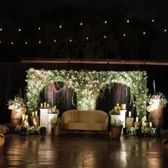 This rustic and romantic stage was designed for an engagement celebration. The backdrop features a lush green arch adorned with white flowers and hanging vines, with pillar candles of varying heights adding a warm, intimate glow.