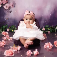 A perfect little poser at her 6-month milestone shoot, surrounded by soft pink flowers.