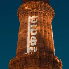 A close-up of the Qutub Minar at night, with projections lighting up its surface. This shot showcases the monument in a modern light, highlighting its intricate details.