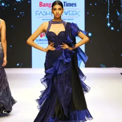 A bold and dramatic ready-to-drape saree in dark blue. This runway piece features voluminous ruffles along the border and a modern, embellished halter-neck blouse, creating a powerful statement look.