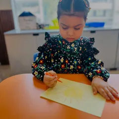 A young artist is completely absorbed in drawing a bright yellow sun. We provide a calm space and quality materials for children to express their creativity.