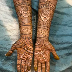 This bridal mehendi showcases symmetrical designs on both hands, featuring peacock motifs and detailed patterns that extend up the forearms. The artistry creates a balanced and harmonious look.