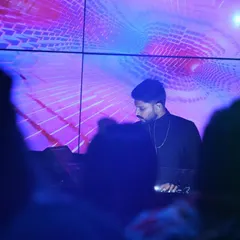 A shot from the crowd's perspective, showing me at the decks against a mesmerizing purple and blue visual display. The goal is to create a complete sensory environment where the music and visuals feel like one.