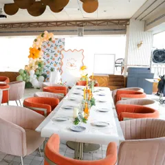 A full view of the baby shower setup, with a long, elegantly set table and comfortable, stylish seating in shades of orange and pink that complement the "cutie" theme.
