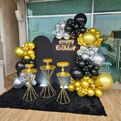 This outdoor terrace setup combines a black backdrop with a balloon arch in gold, silver, and black. The neon "Happy Birthday" sign and gold cake stands complete the look for a stylish evening celebration.