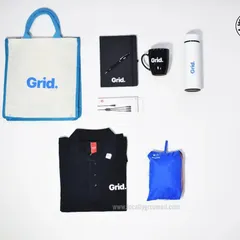 A comprehensive onboarding kit for Grid, featuring a branded polo shirt, a jute tote bag, a notebook and pen, a mug, a water bottle, and a rain poncho. This shows the variety of items we can source and brand for a complete welcome package.