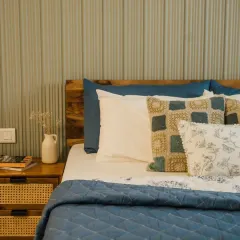 A close-up of a perfectly layered bed. This look combines a solid blue quilted coverlet, a crisp white pillow, and our custom cushion covers in complementary patterns and textures, creating a cozy and inviting sleep space.