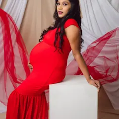 Slaying in bold red. This studio shot showcases a powerful and confident pose, with the vibrant red dress beautifully highlighting the baby bump against a simple, elegant backdrop.