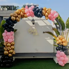 A full view of the chic outdoor balloon arch for a bachelorette party, using a modern color palette of black, pink, and gold.