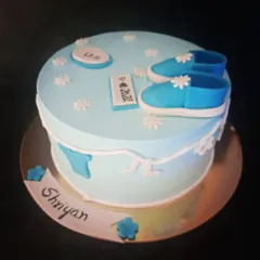 A lovely blue cake for a baby's naming ceremony. It's decorated with tiny shoes and flowers, and includes a plaque with the baby's name and date.