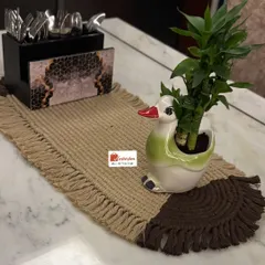 This two-tone table runner, in natural beige and rich brown, adds a touch of handcrafted elegance to your dining table. It's shown here styled with a cutlery holder and a small plant.