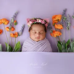 Dreaming in a field of flowers. This artistic setup places a peacefully sleeping newborn among lavender and poppy props, creating a beautiful, colorful, and imaginative portrait.