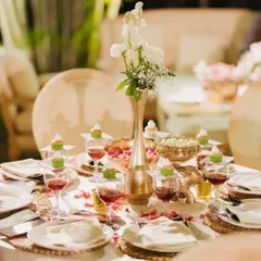 An exquisite table setting for a 75th anniversary dinner. The elegant white and gold theme is complemented by delicate floral centerpieces and individual cupcakes for each guest.