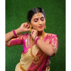 A candid moment of a bride getting ready. This shot highlights the harmony between the pink-toned eyeshadow, the cream and pink Kanjivaram saree, and the traditional gold temple jewellery.