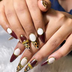 For the client who dares to be different. This set features sharp, stiletto extensions with a mix of deep burgundy, hand-painted leopard print, and a unique white 'negative space' design framed in gold.