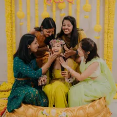 The bride's friends playfully apply Haldi to her face, her laughter capturing the fun and festive spirit of the ceremony.