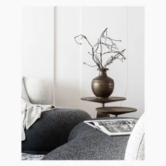 A detail shot of a living room where form meets flow. The sculptural black boucle seating is contrasted with a smooth, tiered side table and a brass vase holding delicate branches, creating a dynamic yet harmonious composition.