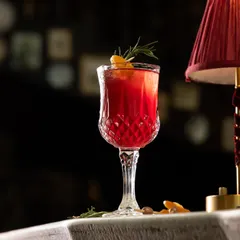 A symphony of flavors in every glass. This deep red cocktail, garnished with rosemary and orange, is a perfect example of the indulgent, handcrafted creations from our bar.