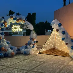 A 30th birthday celebration on a terrace at night. This setup features a balloon arch, a "Happy Birthday" neon sign, and a cozy tent illuminated with fairy lights.