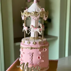 A fairytale spinning to life for a little one's first birthday. This two-tier carousel cake, with its delicate pink fondant, handcrafted horses, and intricate gold details, is a perfect example of the whimsical magic we love to create for childhood celebrations.