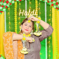 A happy client at her Haldi ceremony, wearing a bright yellow floral jewellery set. The set includes a maang tikka, earrings, and haath phool with delicate hanging flowers.
