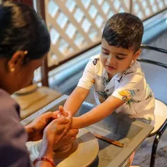 A young boy fully focused on his pottery session, learning to shape the clay with gentle guidance.